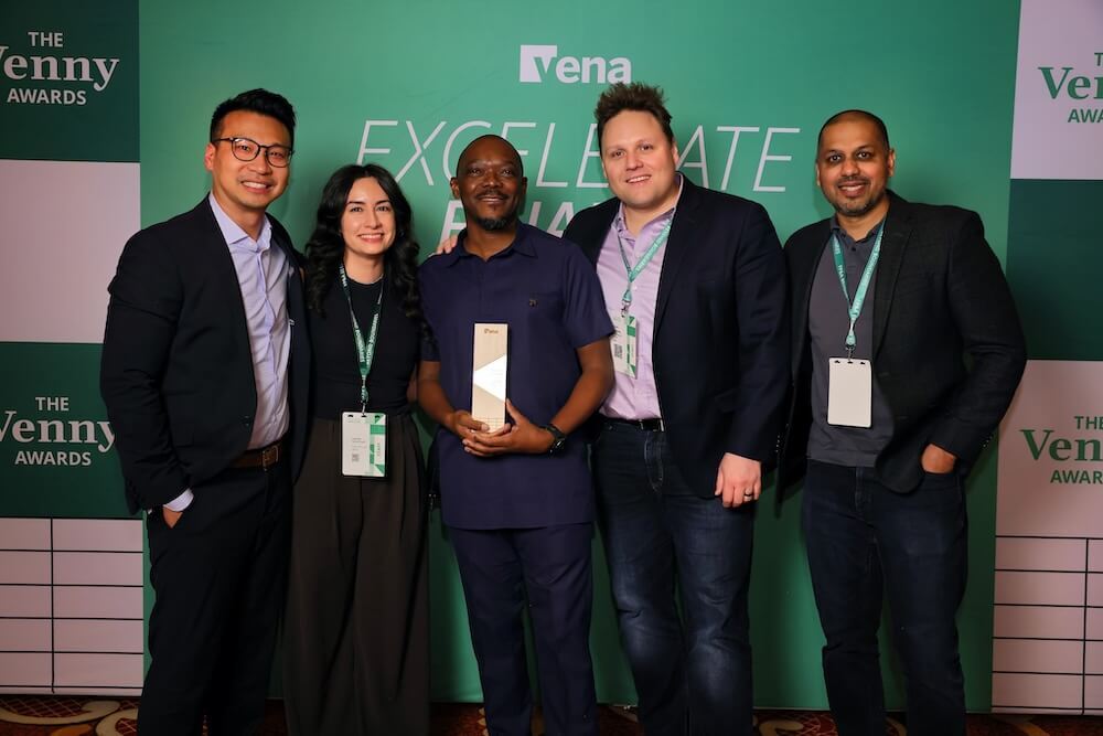 Five people pose at a Vena event; center person holds a trophy in front of a green backdrop.